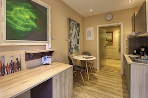 Quarto de hotel com escrivaninha de madeira, mesa redonda, cozinha e obras de arte nas paredes.