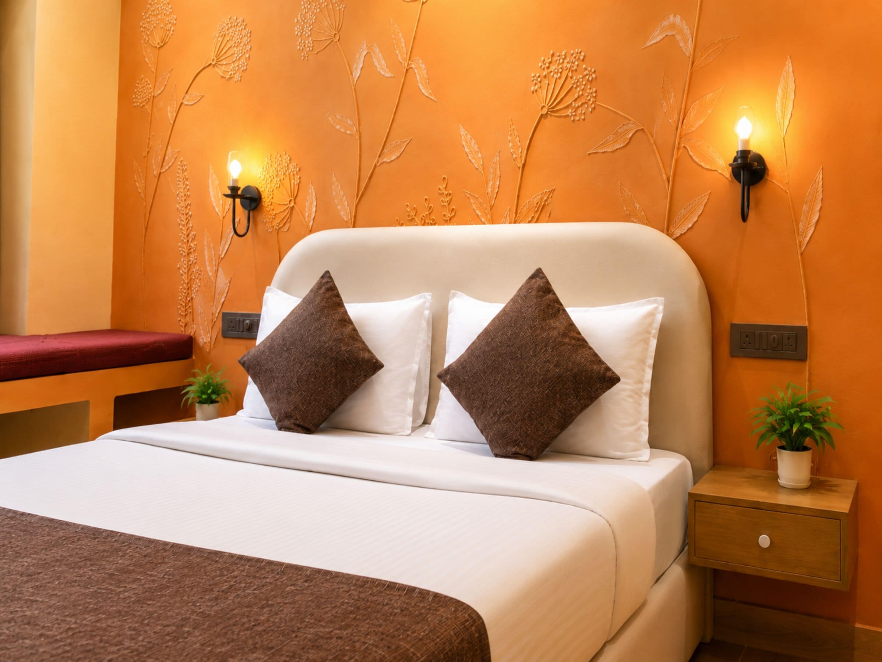 A hotel room with a bed, two wall-mounted lights, a nightstand, and a red bench.