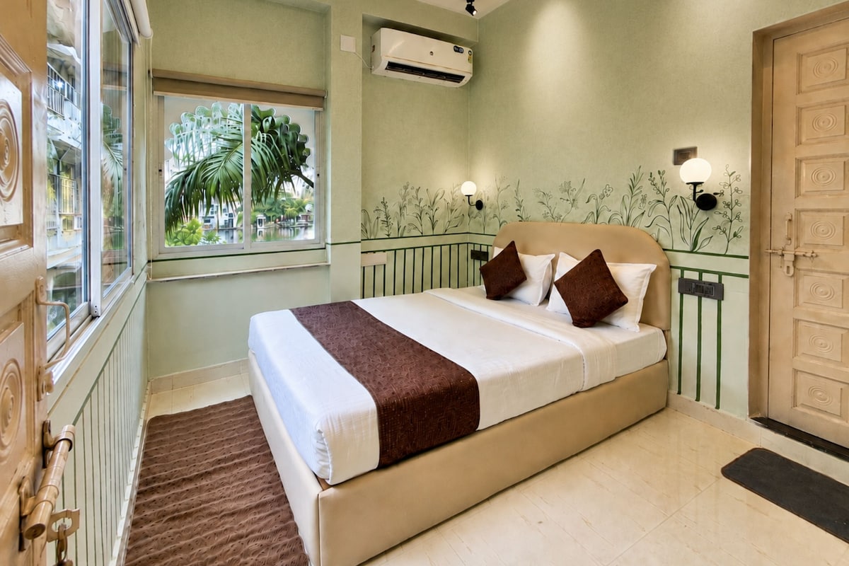A bedroom with a bed, a window, an air conditioning unit, and a door.