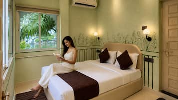 A room with a bed, a window with a view of palm trees, an air conditioning unit, and wall-mounted lights.