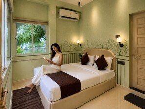 A room with a bed, a window with a view of palm trees, an air conditioning unit, and wall-mounted lights.