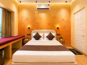 Quarto de hotel com cama, mesas de cabeceira, aparelho de ar condicionado, guarda-roupa e um banco.