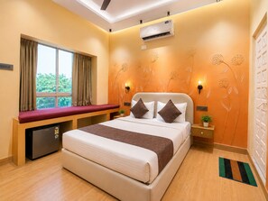 Quarto de hotel com cama, um banco, aparelho de ar condicionado, janela com cortinas e parede com arte floral.