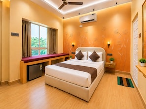 A hotel room with a bed, a desk, a window with curtains, an air conditioner, and a ceiling fan.