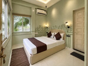 A bedroom with a bed, a window, an air conditioning unit, and a door.