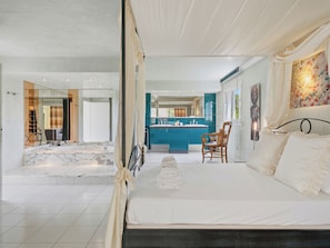 Een moderne hotelkamer met een groot bed, een zithoek met een stoel, een badkamer met een grote spiegel en uitzicht op buiten.