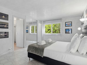 A bedroom with a bed, a window with a view of greenery, a door leading to another room, and framed pictures on the wall. - Villa KeyWest - 4 Etoiles - 3 Suites - Piscine 14m - Gym (Villetelle)