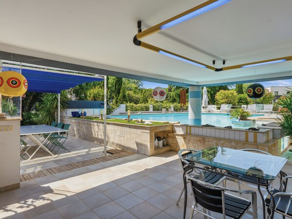 Area piscina con tavolo e sedie, piscina e zona relax coperta.