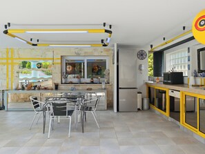 A modern kitchen with a central island, stainless steel appliances, and a dining area with metal chairs. - Villa KeyWest - 4 Etoiles - 3 Suites - Piscine 14m - Gym (Villetelle)
