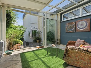 A conservatory with a glass door, a small table, a sofa, and a potted plant. - Villa KeyWest - 4 Etoiles - 3 Suites - Piscine 14m - Gym (Villetelle)