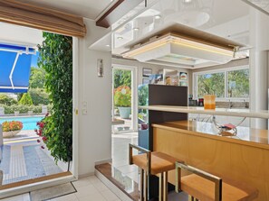 Een moderne keuken met een bar, een groot raam met uitzicht op het zwembad, en een deur naar een balkon.