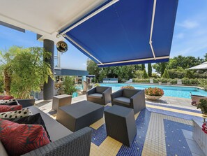 Een overdekt terras met rieten meubilair en een zwembad op de achtergrond.