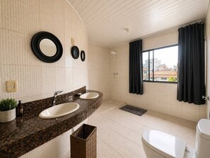Ein Badezimmer mit zwei Waschbecken, Toilette, Dusche und einem Fenster mit Vorhängen.