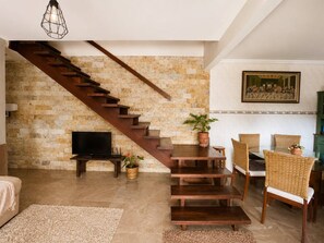 Una sala de estar moderna con una escalera de madera, un televisor de pantalla plana, mobiliario de mimbre y un cuadro en la pared.