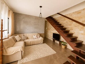 Ein modernes Wohnzimmer mit einer Eckcouch, einem Flachbildfernseher, einer Holztreppe und einer Steinwand.