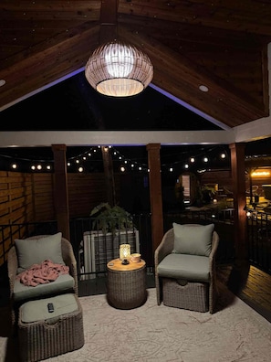 An outdoor seating area with wicker chairs, a round table, and string lights. - Couples Reconnect & Rejuvenate. (Lonoke County)