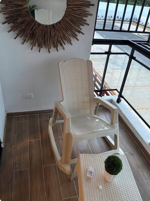 Quarto com uma cadeira branca, uma pequena mesa com uma planta e um espelho fixado na parede.