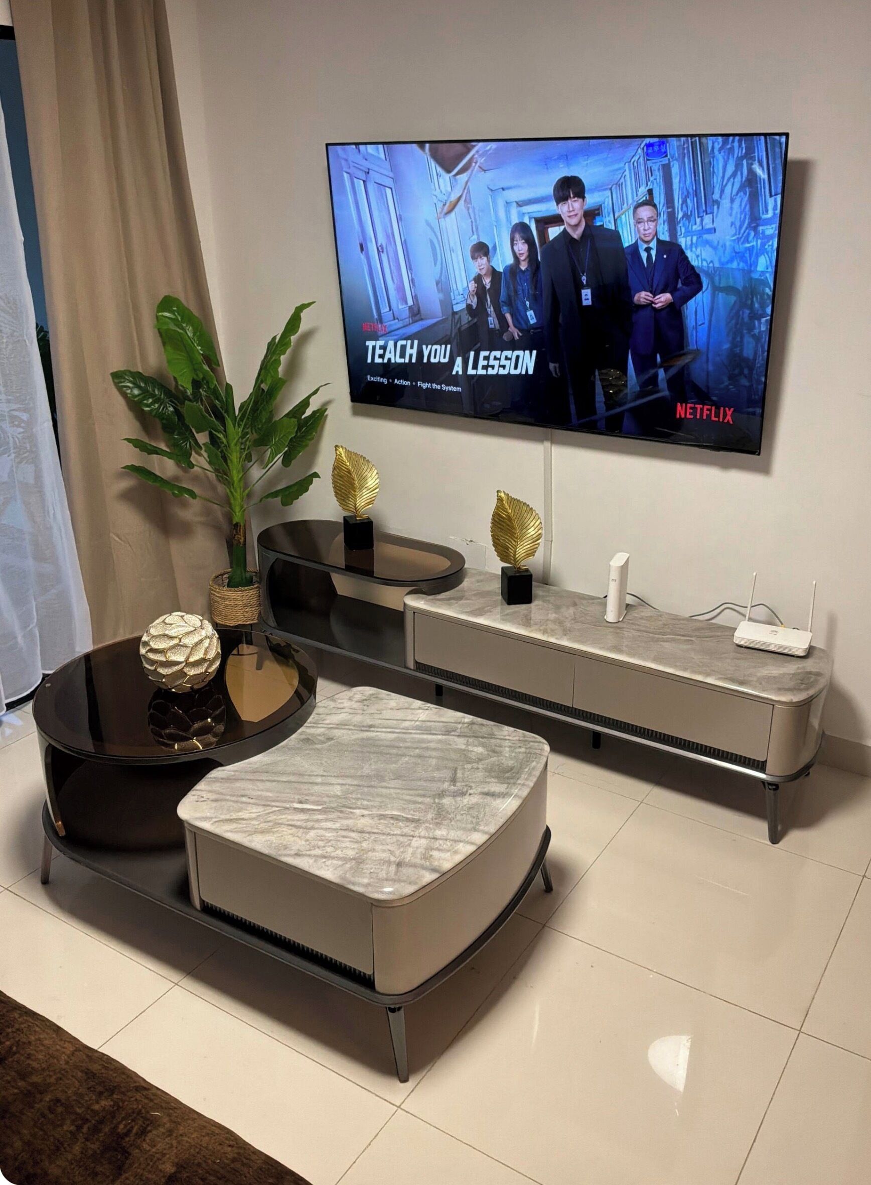 Una sala de estar moderna con un televisor de pantalla plana montado en la pared, una mesa de centro de vidrio, un reposapiés de mármol y un mueble de entretenimiento minimalista.