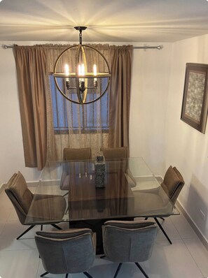 Ein Esszimmer mit einem Glastisch, umgeben von Stühlen, einer Kandelaber und Vorhängen.