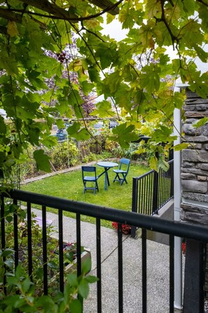 A garden patio with a stone wall, a small table, two blue chairs, and a view of a residential area with trees and a house.