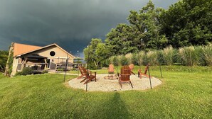 A house with a covered patio, outdoor seating, and a view of a forested area. - Cozy 4-bedroom cabin in tranquil Newcomerstown with AC (Newcomerstown)