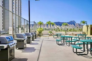Eine Terrasse im Freien mit Grillanlagen, Tischen und Stühlen, mit Blick auf eine Berglandschaft.