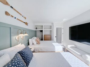 Ein Hotelzimmer mit zwei Betten, einem Fernseher, einem Kleiderschrank und einem Schreibtisch mit Lampe.