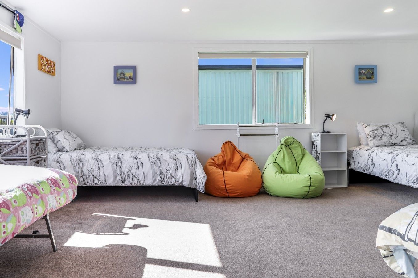 A bedroom with a bed, two bean bags, a desk, and a window with blinds.