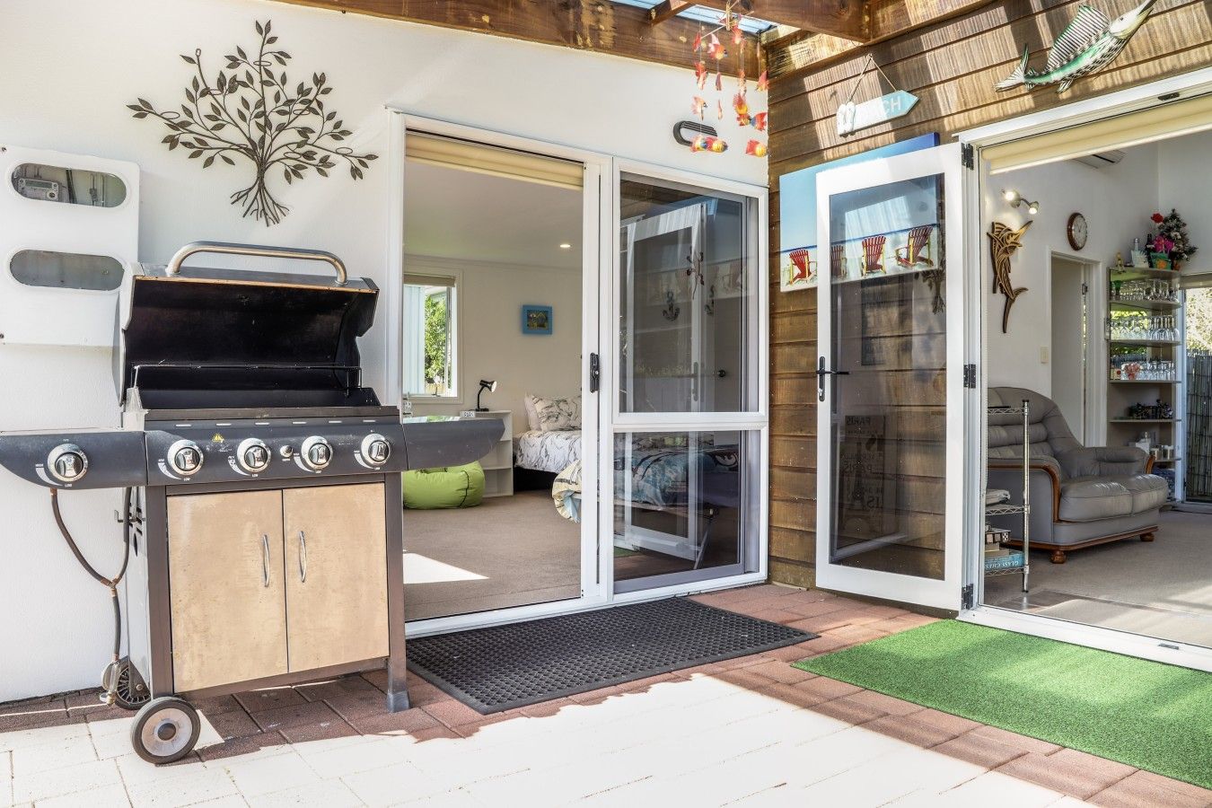 Een buitenkeuken met een grill, schuifdeuren naar een woonkamer en een klein terras met kunstgras.
