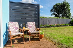 An outdoor seating area with two wooden chairs and a table, a bottle of champagne, and a glass.