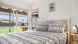 Un dormitorio con una cama grande, una mesita de noche, un letrero de vino en la pared y vistas al exterior.