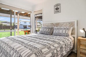 Una camera da letto con un letto grande, un comodino, un cartello a muro con la scritta vino e vista sull'esterno.