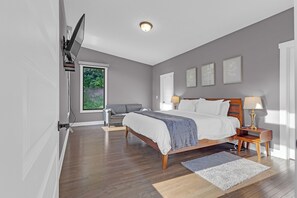 Un dormitorio con una cama, mesitas de noche, un ventanal y una puerta.
