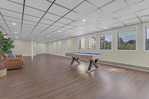 Ein geräumiges Zimmer mit Billardtisch, einer Ledersofa und großen Fenstern mit Blick ins Freie.
