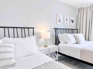 Quarto de hotel com duas camas, uma mesa de cabeceira com abajur e uma obra de arte na parede.