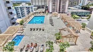 Ein Poolbereich auf dem Dach mit mehreren Pools und Liegestühlen, umgeben von Hochhäusern.