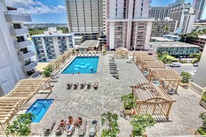 Uma área de piscina no terraço, com várias piscinas e espreguiçadeiras, cercada por edifícios altos.
