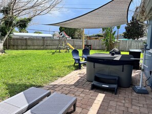 Ein Garten mit einer Terrasse, einem Whirlpool und einer Schaukel.