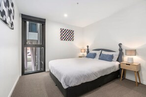 A bedroom with a bed, two bedside tables, a window, and a wall art piece. - Modern Apartment near Hospital, Geelong (Greater Geelong)