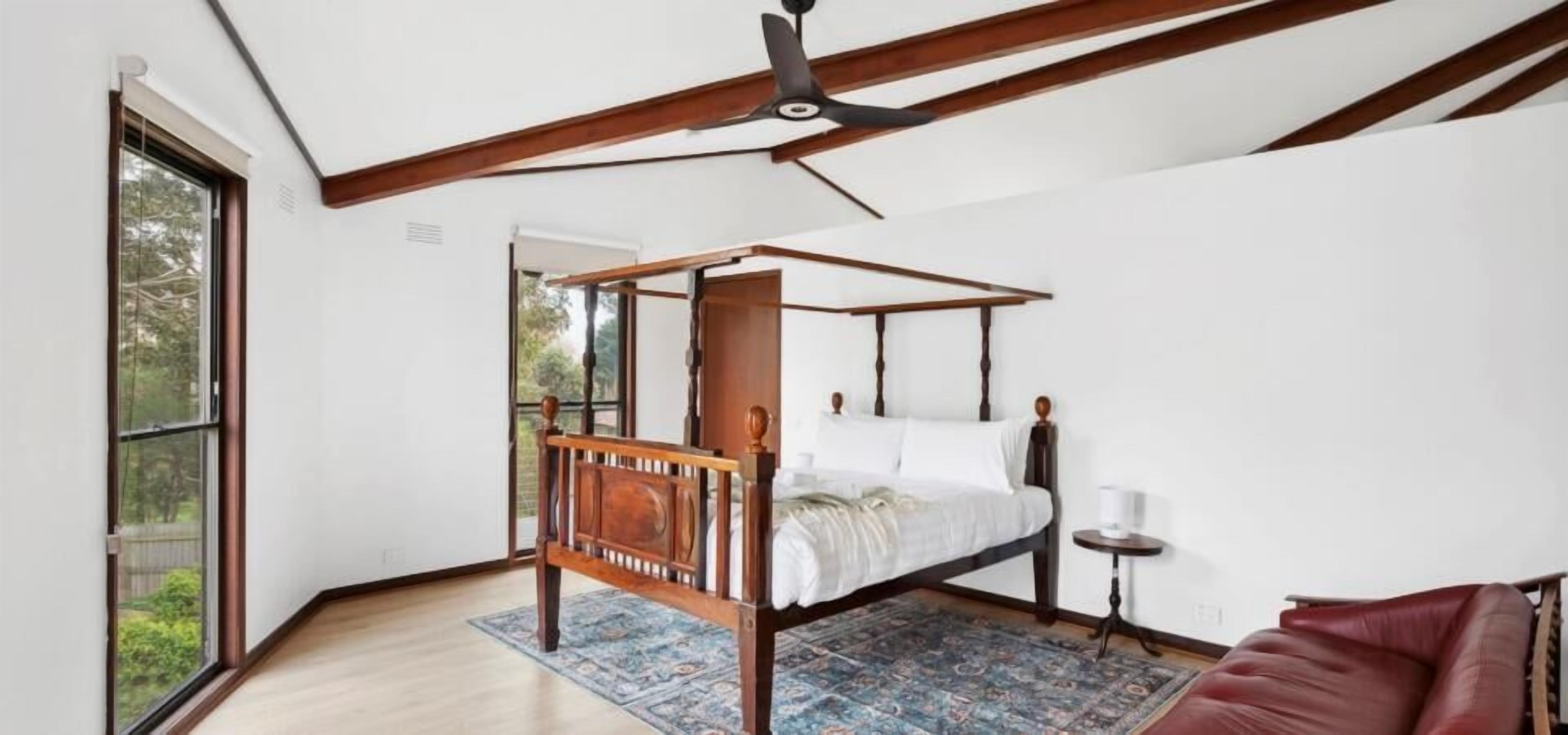 Ein Schlafzimmer mit einem Himmelbett, Deckenventilator, einem Fenster und einem roten Ledersofa.