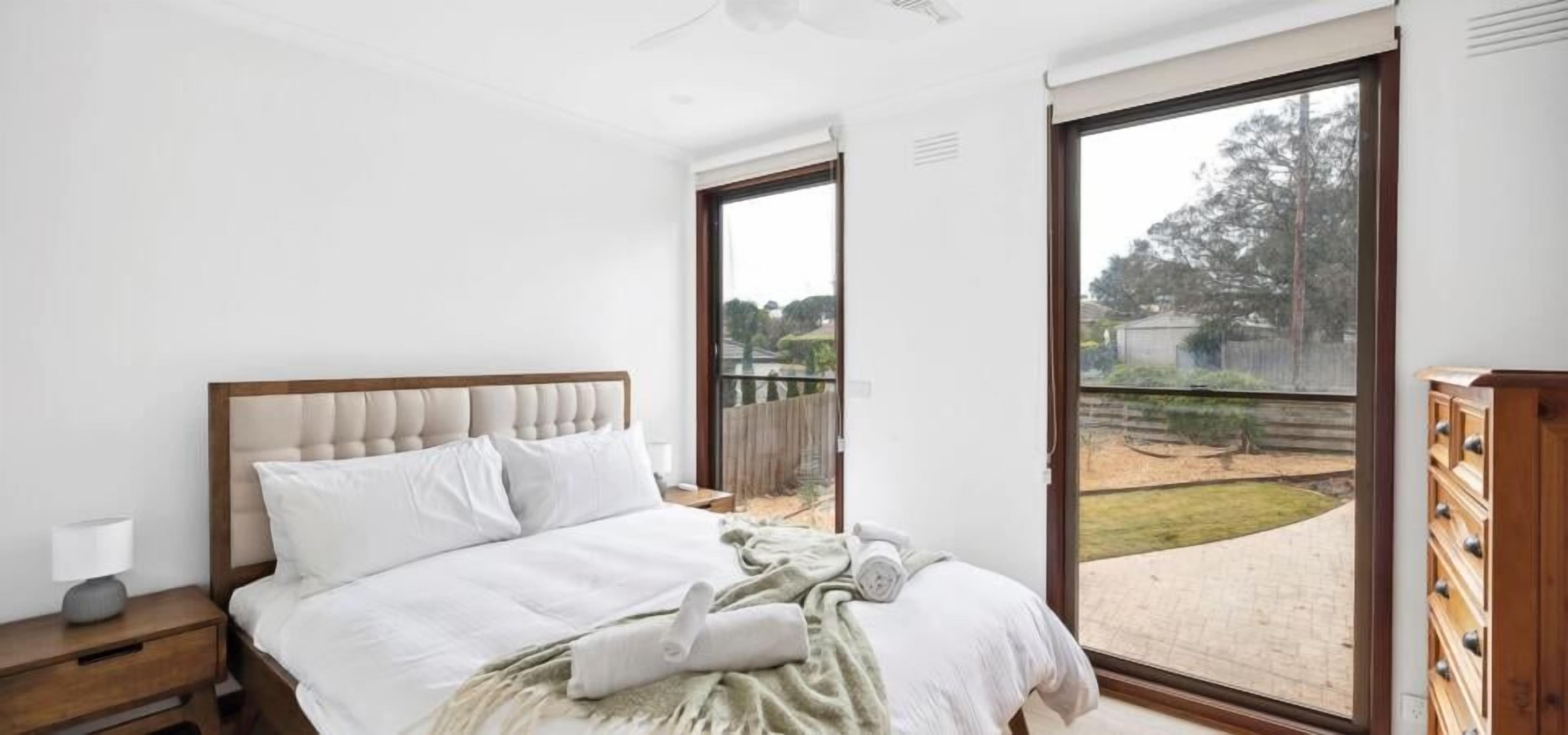 A bedroom with a bed, a nightstand, a dresser, and a sliding glass door leading to a backyard.