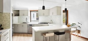 A modern kitchen with a central island, pendant lighting, and a view to the outside. - Family-Friendly Renovated 4BR Clifton Retreat (Greater Geelong)