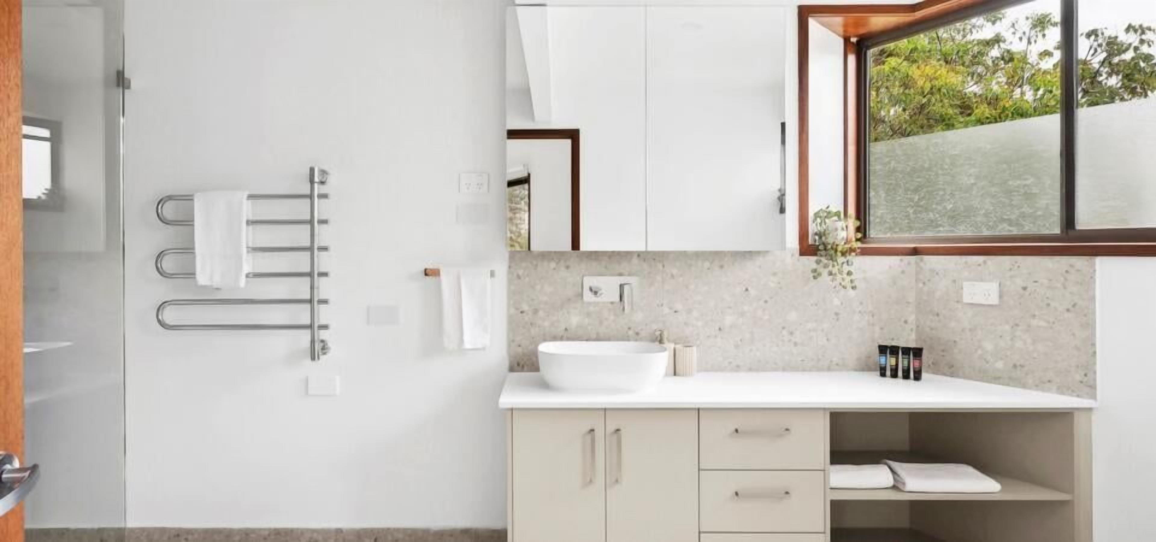 Een moderne badkamer met een groot raam, een witte wastafel en een handdoekhouder.