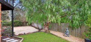 A backyard with a wooden fence, a statue, and a tree with green foliage. - Family-Friendly Renovated 4BR Clifton Retreat (Greater Geelong)