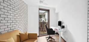 Una sala de estar moderna con una pared de ladrillo blanco, un sofá, un escritorio con una computadora y vistas a través de un vidrio.