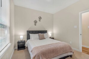 Een slaapkamer met een bed, nachtkastjes, een kunstwerk aan de muur en een raam met jaloezieën.