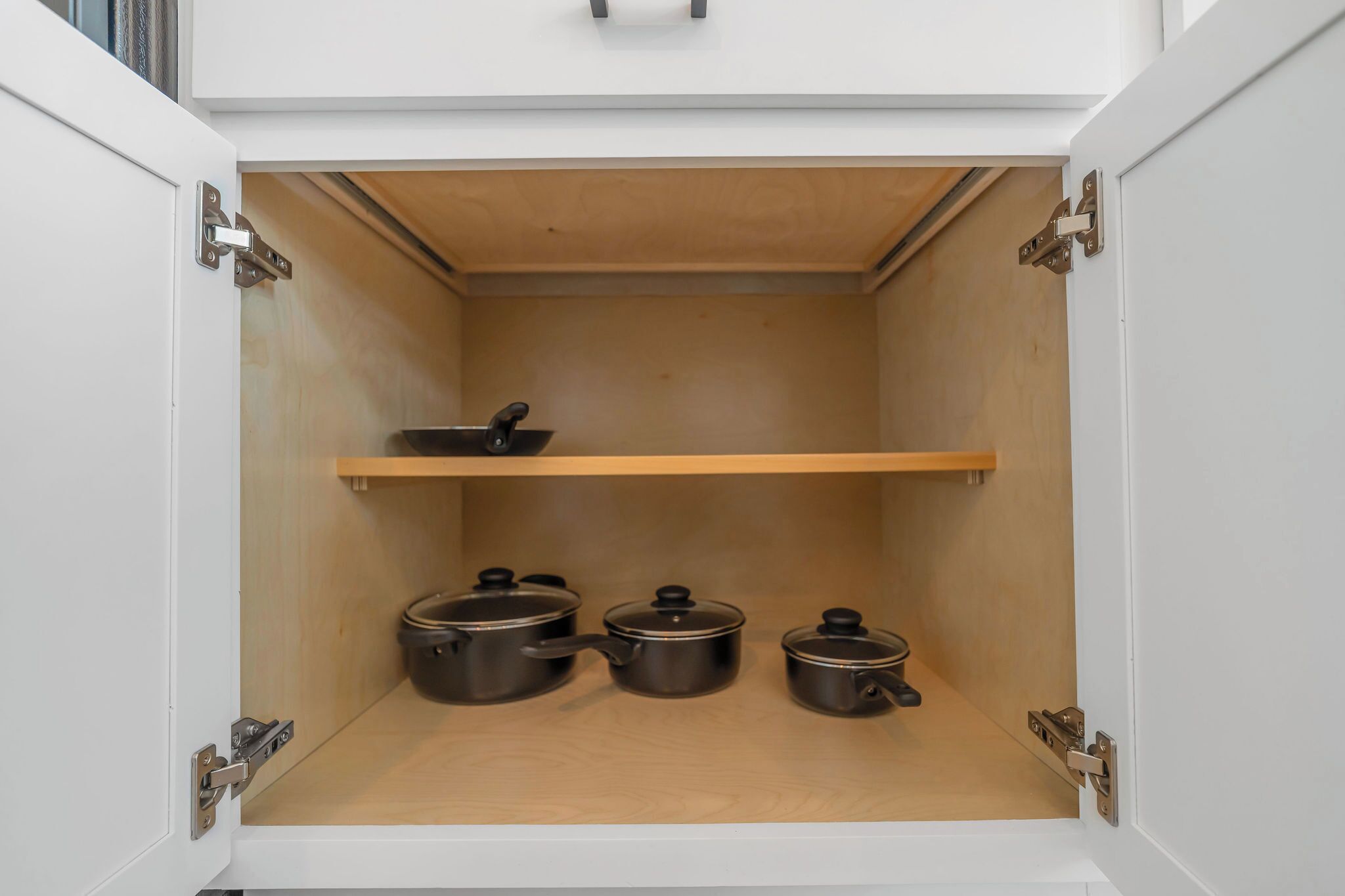Un meuble de cuisine avec trois casseroles sur l’étagère inférieure et une poêle sur l’étagère supérieure.