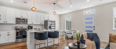 A modern kitchen with white cabinets, stainless steel appliances, and a bar area with stools.