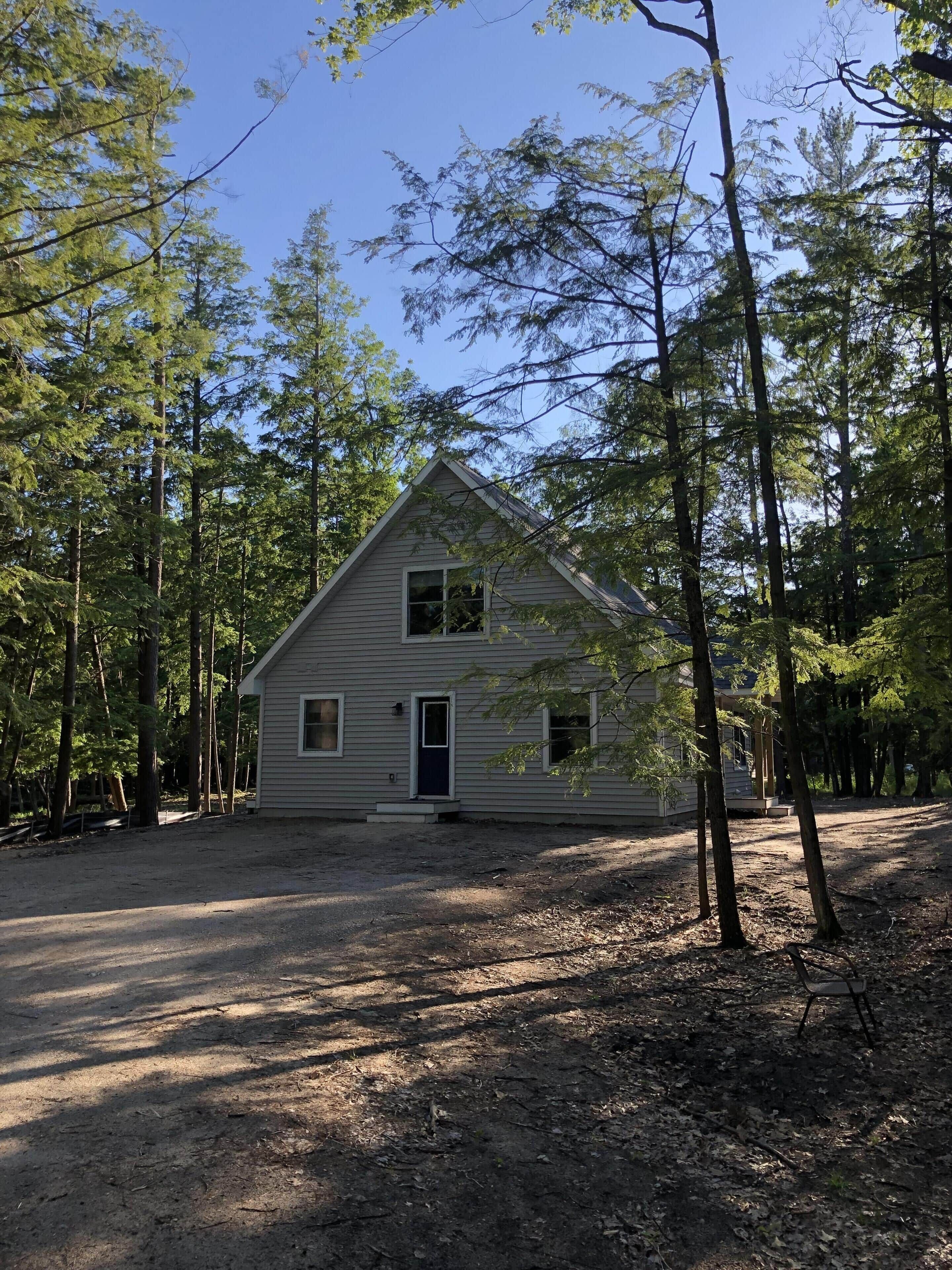 Une cabane de plain-pied, dotée d’un toit à pignon, entourée de grands arbres.