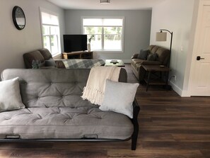 Ein Wohnzimmer mit einem grauen Sofa, einem braunen Sofa, einem Couchtisch und einem Fernseher auf einem Lowboard.